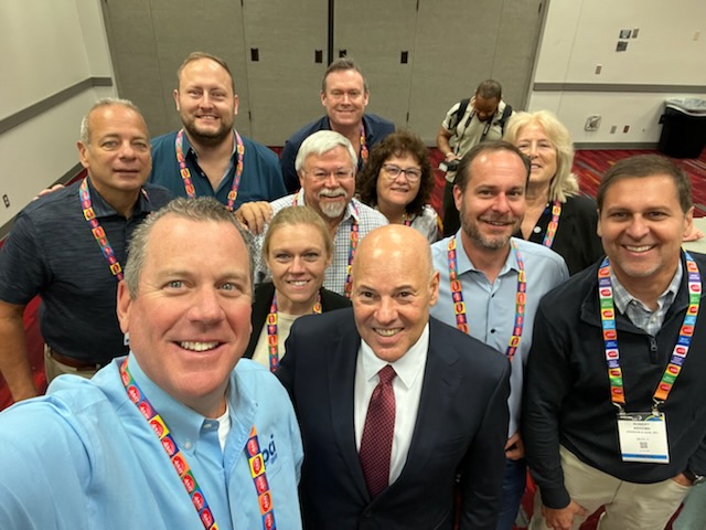 A group of PrintMail employees and the Postmaster General pose for a selfie picture during a meeting